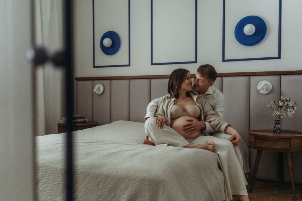 Para podczas domowej sesji ciazowej w sypialni w Warszawie - tata szepcze do ucha mamie z brzuszkiem - Magda Zaborowska Fotografia